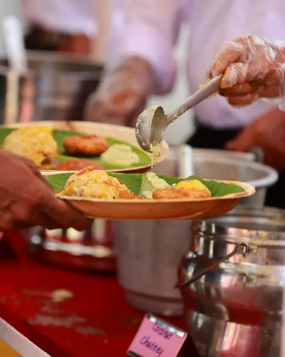 A Yuvah Caterers server spooning food onto a guest's plate at a buffet